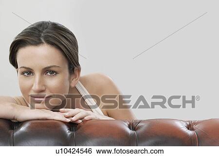 Stock Photograph - Portrait of beautiful woman on sofa against gray background. Fotosearch