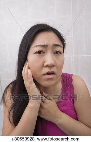 Stock Photo - Portrait of beautiful young woman examining her face in bathroom. Fotosearch