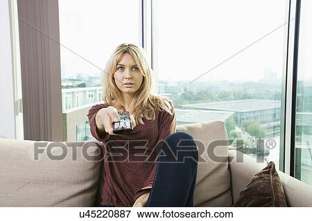 Portrait of blue eyed woman watching television on sofa at home View Large Photo Image Stock Photo - Portrait of blue eyed woman watching television on sofa at home. Fotosearch