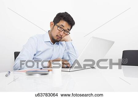 Portrait of bored businessman sitting with laptop at desk in office View Large Photo Image Picture - Portrait of bored businessman sitting with laptop at desk in office. Fotosearch
