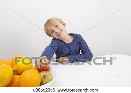 Portrait of boy holding apple from fruit bowl at table View Large Photo Image Stock Photograph - Portrait of boy holding apple from fruit bowl at table. Fotosearch