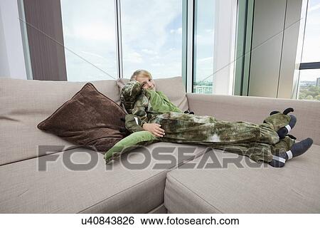 Stock Photograph - Portrait of boy wearing dinosaur costume relaxing on sofa at home. Fotosearch