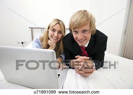 Stock Photo - Portrait of business couple with laptop lying on bed. Fotosearch