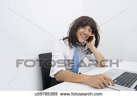 Portrait of businessman wearing wig while using cell phone in office View Large Photo Image Stock Photo - Portrait of businessman wearing wig while using cell phone in office. Fotosearch
