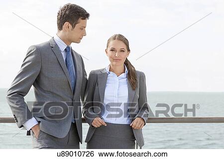 Stock Photograph - Portrait of businesswoman with coworker leaning on terrace railing against sky. Fotosearch