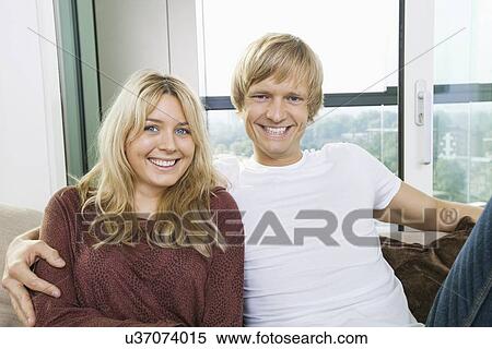Portrait of cheerful couple sitting on sofa at home View Large Photo Image Stock Photography - Portrait of cheerful couple sitting on sofa at home. Fotosearch
