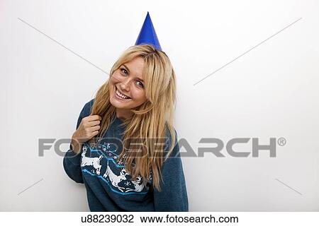 Stock Image - Portrait of cheerful woman wearing party hat against white background. Fotosearch