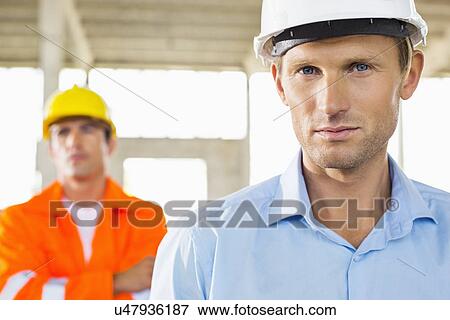 Portrait of confident architect at construction site with coworker in background View Large Photo Image Stock Photo - Portrait of confident architect at construction site with coworker in background. Fotosearch