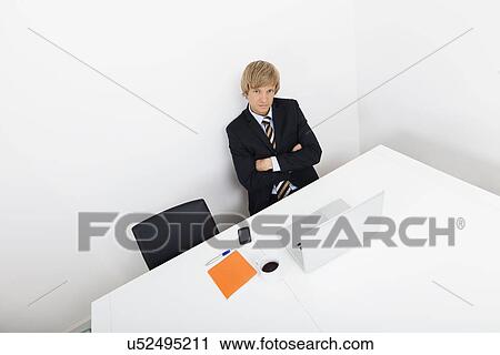 Stock Image - Portrait of confident businessman sitting at desk with laptop. Fotosearch