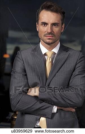 Stock Photo - Portrait of confident businessman standing arms crossed in office. Fotosearch