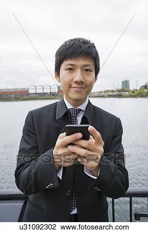 Stock Image - Portrait of confident businessman text messaging through cell phone outdoors. Fotosearch