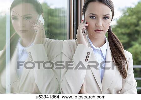Picture - Portrait of confident businesswoman answering cell phone by glass door. Fotosearch