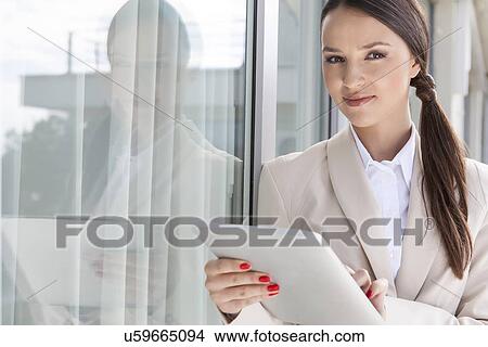 Portrait of confident businesswoman using digital tablet by glass door View Large Photo Image Picture - Portrait of confident businesswoman using digital tablet by glass door. Fotosearch