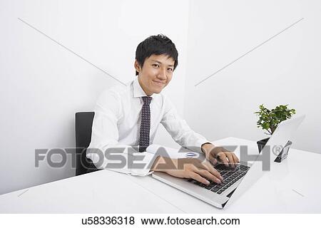 Stock Photo - Portrait of confident mid adult businessman using laptop at office desk. Fotosearch