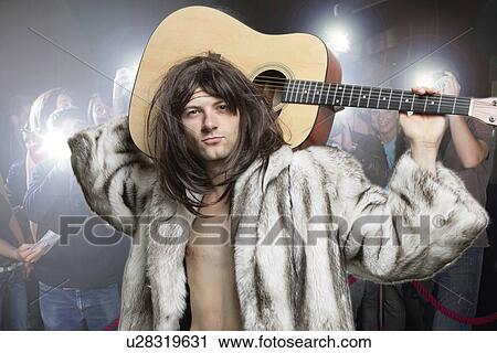 Stock Image - Portrait of confident rockstar being photographed by paparazzi. Fotosearch