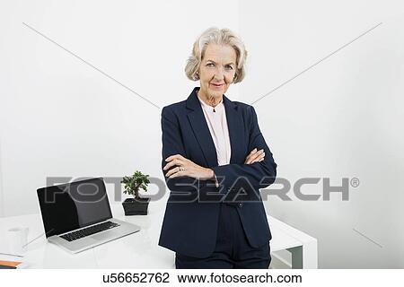 Stock Image - Portrait of confident senior businesswoman with arms crossed in office. Fotosearch