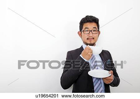 Stock Image - Portrait of confident young businessman holding coffee cup and plate over white background. Fotosearch