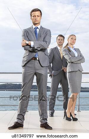 Stock Photo - Portrait of confident young businessman standing with coworkers on terrace against sky. Fotosearch