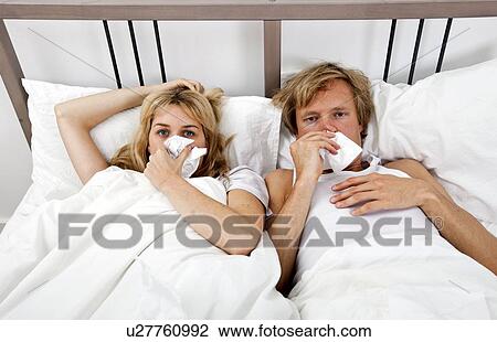 Stock Image - Portrait of couple suffering from cold lying on bed. Fotosearch