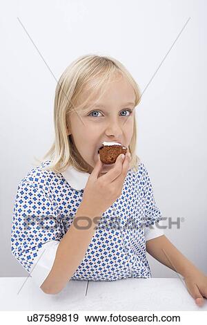 Stock Photo - Portrait of cute girl eating muffin at table in house. Fotosearch
