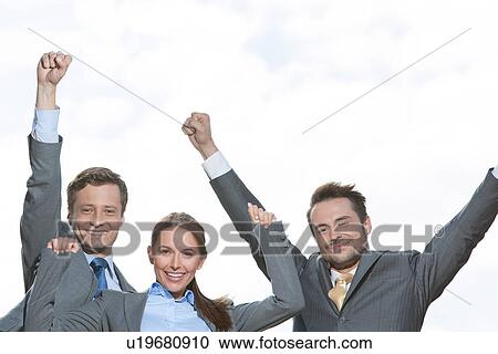 Stock Image - Portrait of excited businesspeople with arms raised on terrace against sky. Fotosearch