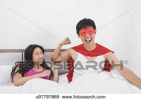 Stock Photo - Portrait of excited man in superhero costume with woman on bed. Fotosearch