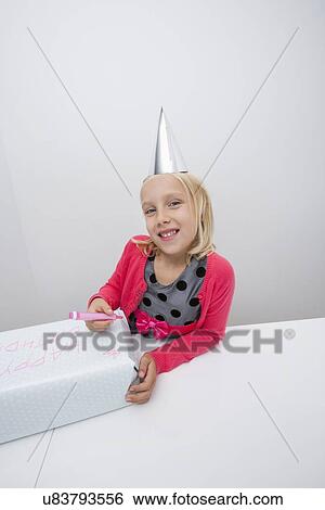 Stock Photograph - Portrait of girl preparing birthday gift at table in house. Fotosearch