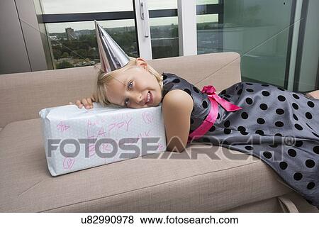 Stock Photo - Portrait of girl with birthday gift lying on sofa at home. Fotosearch