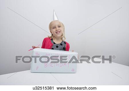 Stock Image - Portrait of girl with birthday present at table in house. Fotosearch