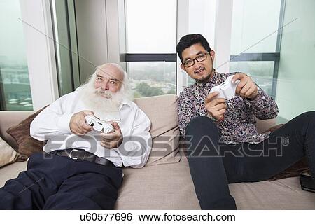 Stock Photograph - Portrait of grandson playing video game on sofa at home. Fotosearch