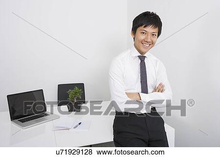 Portrait of happy Asian businessman with arms crossed leaning on office desk View Large Photo Image Stock Photo - Portrait of happy Asian businessman with arms crossed leaning on office desk. Fotosearch