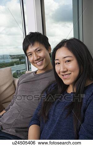 Portrait of happy Asian couple sitting on sofa at home View Large Photo Image Stock Photograph - Portrait of happy Asian couple sitting on sofa at home. Fotosearch