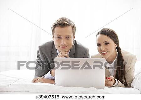 Stock Photograph - Portrait of happy business couple with laptop in hotel. Fotosearch