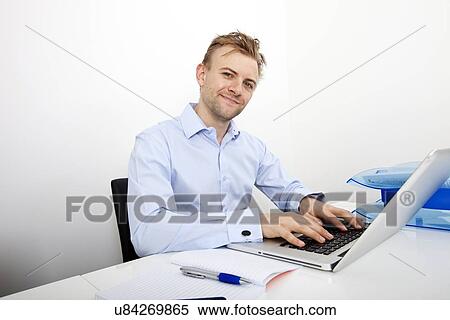 Stock Photography - Portrait of happy businessman using laptop at desk in office. Fotosearch