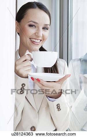 Stock Image - Portrait of happy businesswoman having coffee in office. Fotosearch