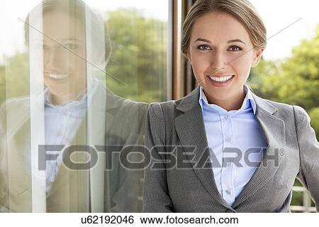 Stock Photograph - Portrait of happy businesswoman leaning on glass door. Fotosearch