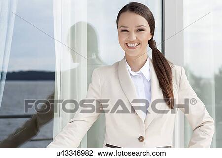Stock Image - Portrait of happy businesswoman standing against glass door. Fotosearch