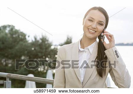 Stock Photo - Portrait of happy businesswoman answering cell phone outdoors. Fotosearch