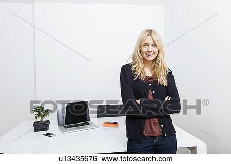 Stock Photograph - Portrait of happy businesswoman standing arms crossed in office. Fotosearch