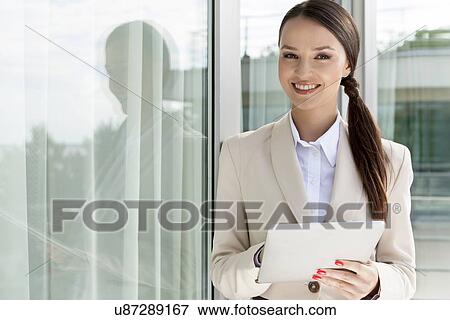 Stock Photo - Portrait of happy businesswoman using digital tablet by glass door. Fotosearch