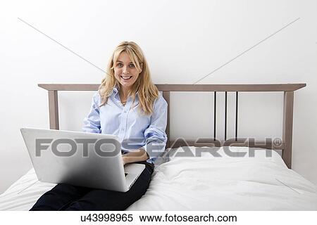 Stock Photography - Portrait of happy businesswoman using laptop in bed. Fotosearch