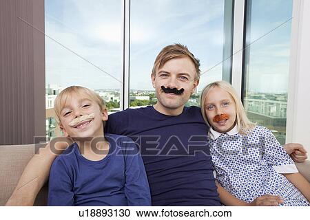 Portrait of happy father and children with artificial mustache sitting on sofa at home View Large Photo Image Stock Image - Portrait of happy father and children with artificial mustache sitting on sofa at home. Fotosearch