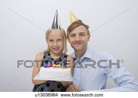 Picture - Portrait of happy man with daughter holding birthday cake against gray background. Fotosearch