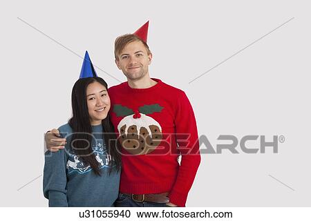 Stock Image - Portrait of happy multiethnic couple wearing party hats at home. Fotosearch