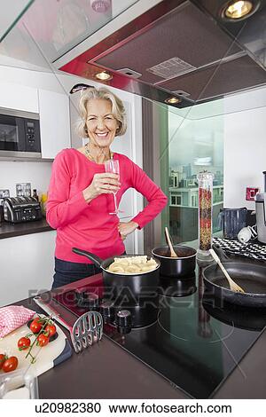 Portrait of happy senior woman with champagne glass cooking food in kitchen View Large Photo Image Stock Image - Portrait of happy senior woman with champagne glass cooking food in kitchen. Fotosearch