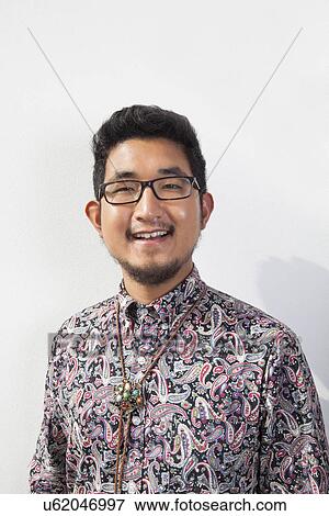 Stock Photo - Portrait of happy young man wearing eyeglasses standing against white background. Fotosearch