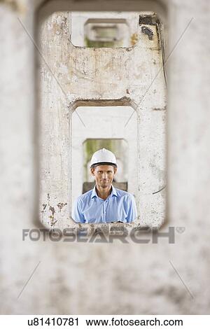Stock Image - Portrait of male architect through pillars at construction site. Fotosearch
