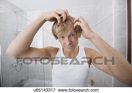 Stock Photo - Portrait of man checking for white hair in bathroom. Fotosearch