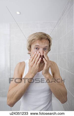 Stock Image - Portrait of man checking for wrinkles on his face in bathroom. Fotosearch