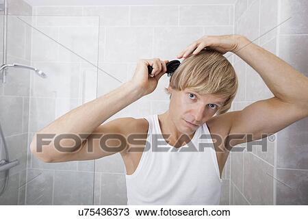 Stock Image - Portrait of man combing hair in bathroom. Fotosearch